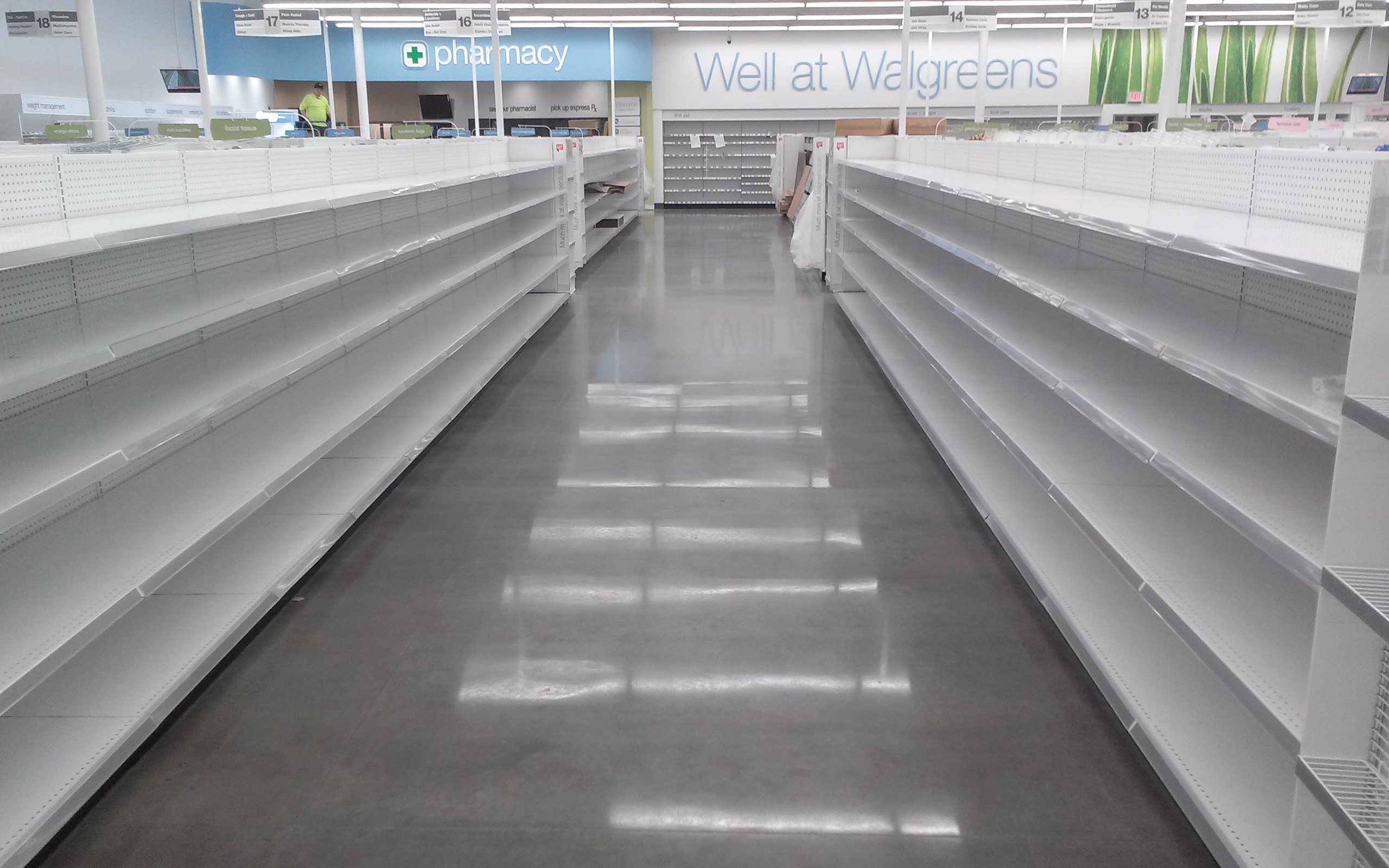 A polished cement floor aisle runs between two white, empty rows in a Walgreens.
